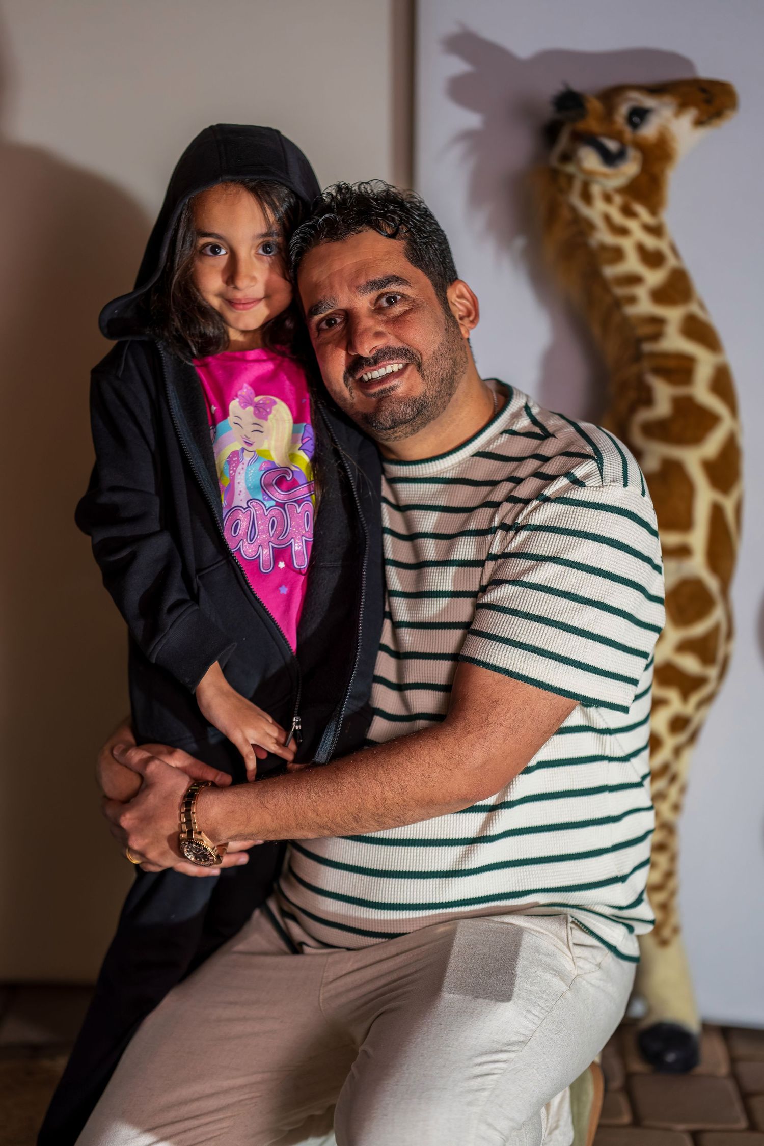 Parent and child pose together in front of decorative giraffe wall art.
