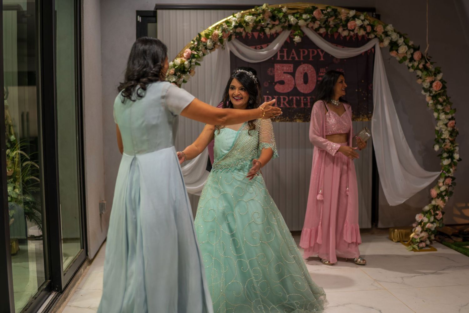 Two people dance together under floral arch at 50th birthday celebration.