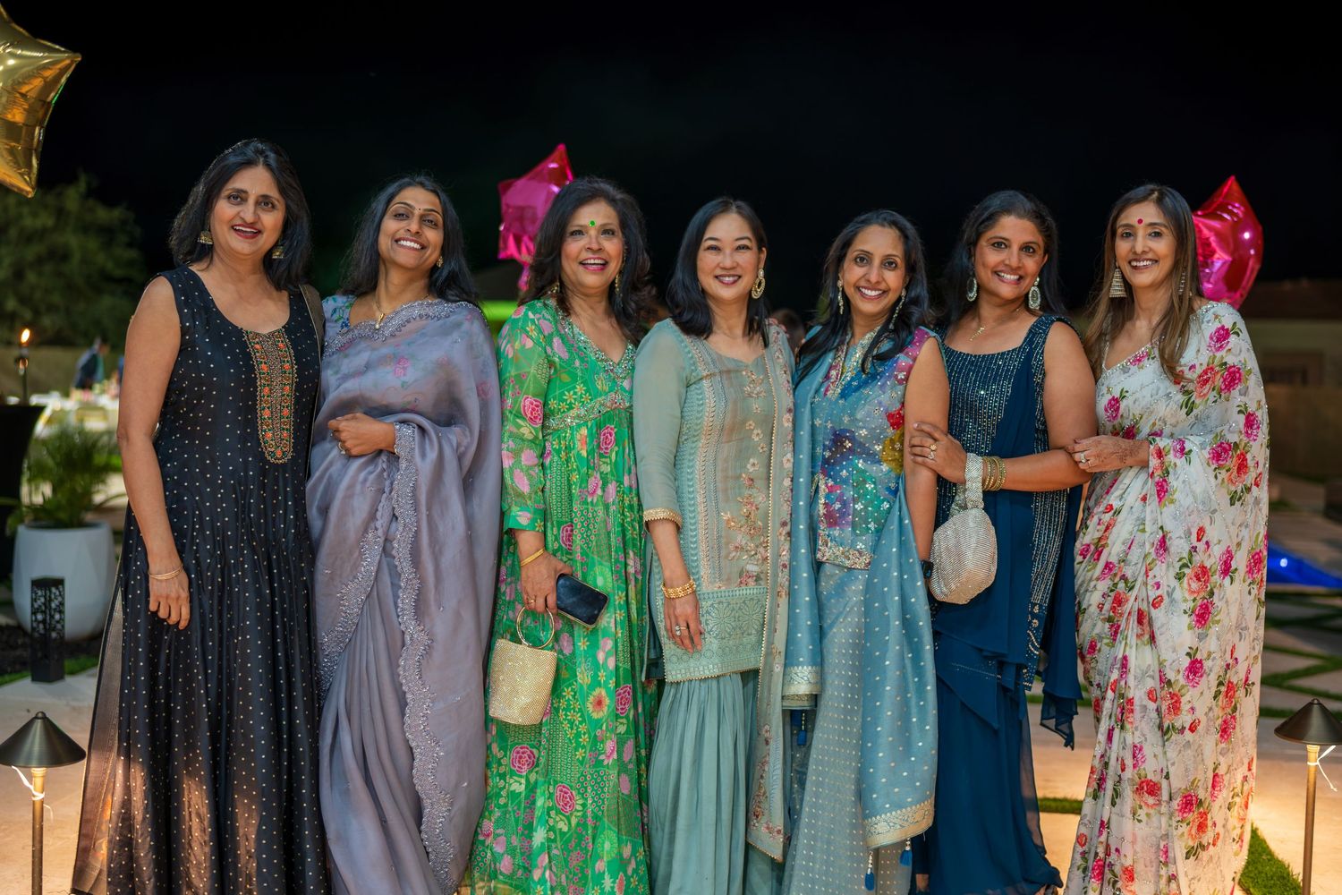 Group of guests in colorful dresses and formal wear gathered for an evening celebration.