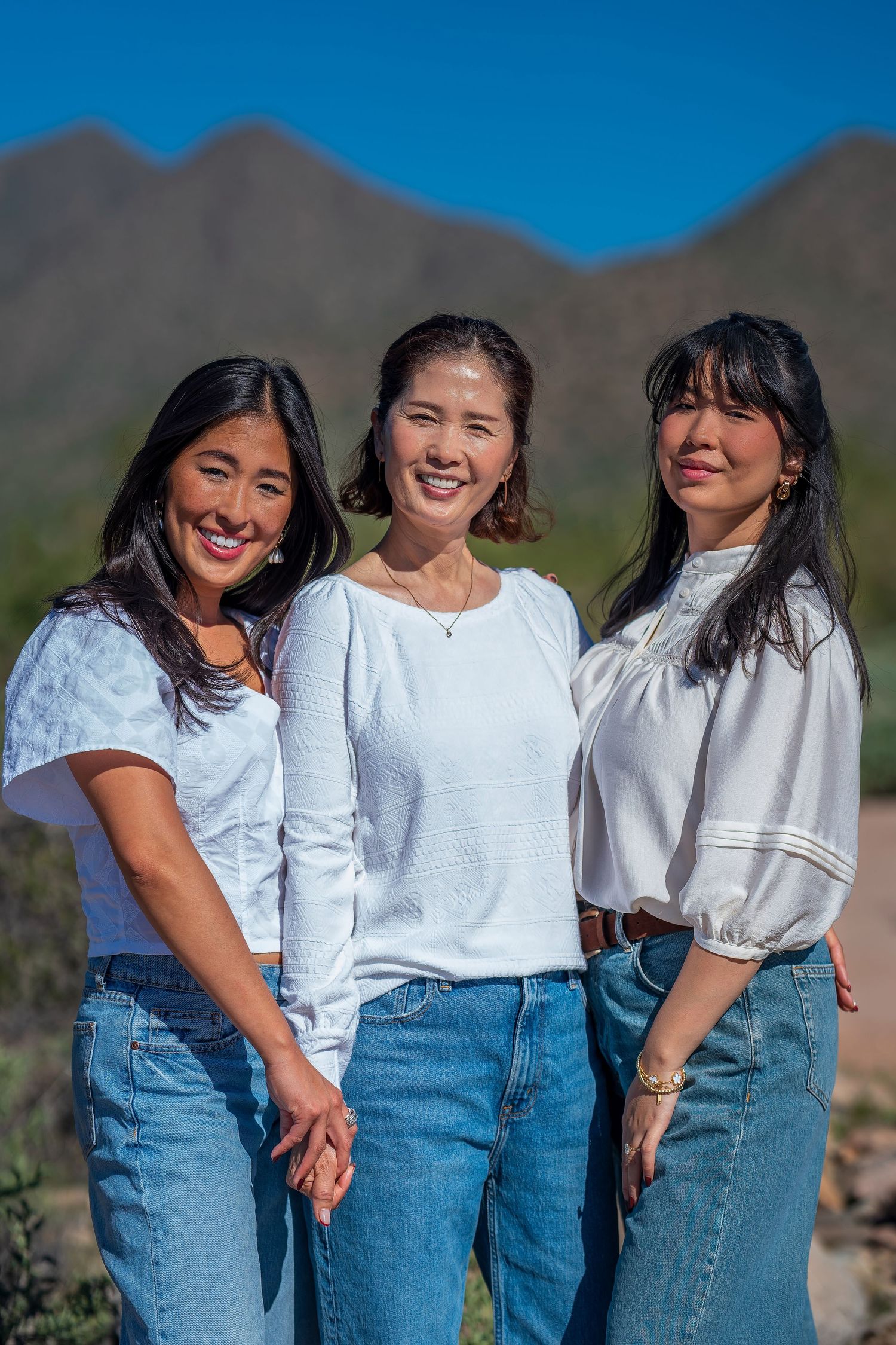 A group wearing matching white tops and blue jeans poses together against a desert mountain backdrop.