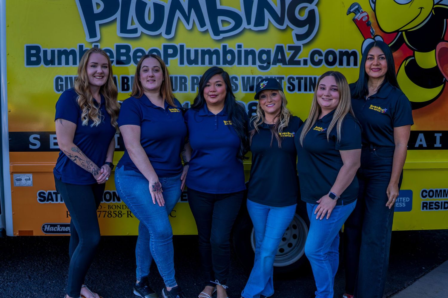 Team members lined up beside yellow Bumble Bee Plumbing truck with company website displayed.