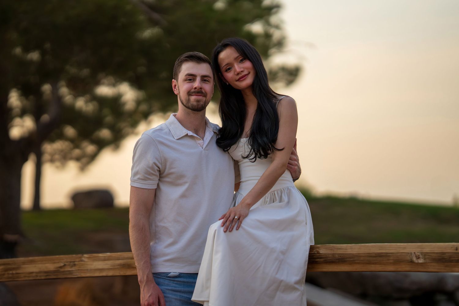 Couple posing at sunset on a wooden bridge, woman in white dress, man in white shirt.