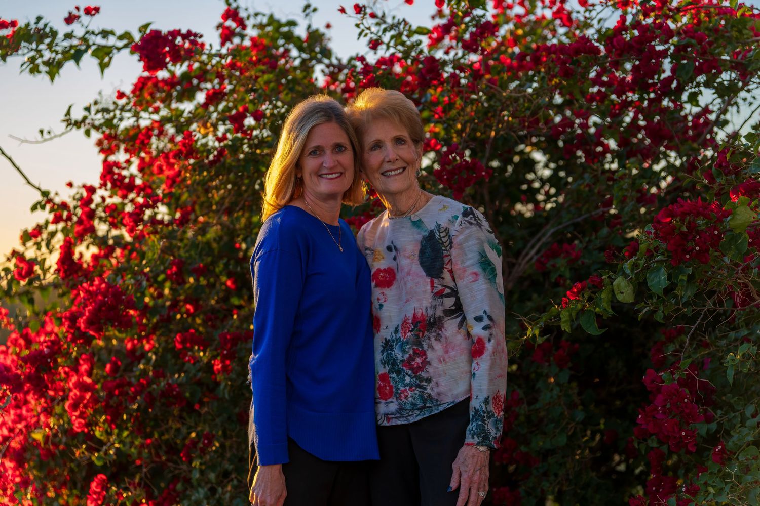 Family portraits with vibrant red flowering bushes in natural outdoor setting.