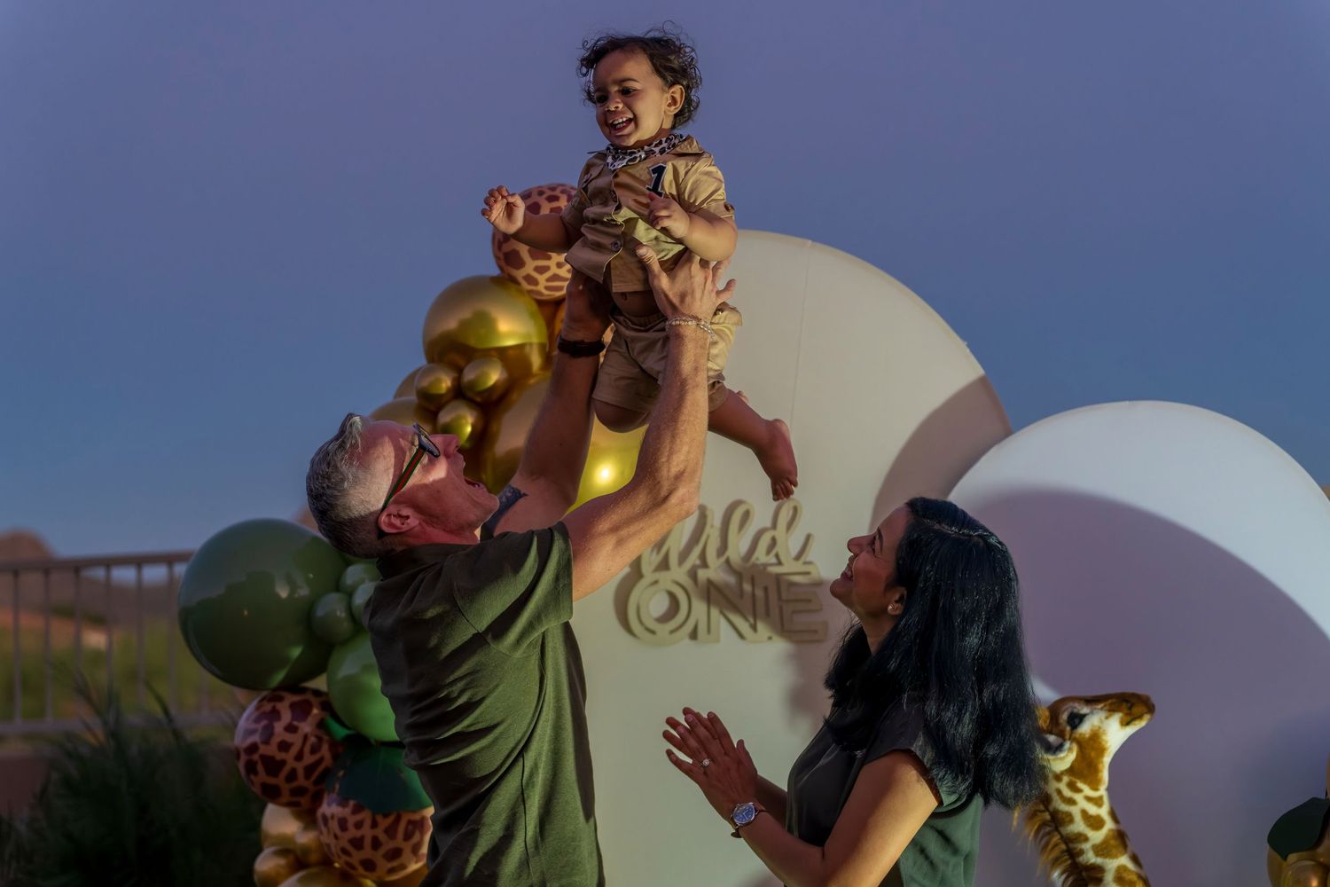Family moment captured during sunset against white curved backdrop with balloons.