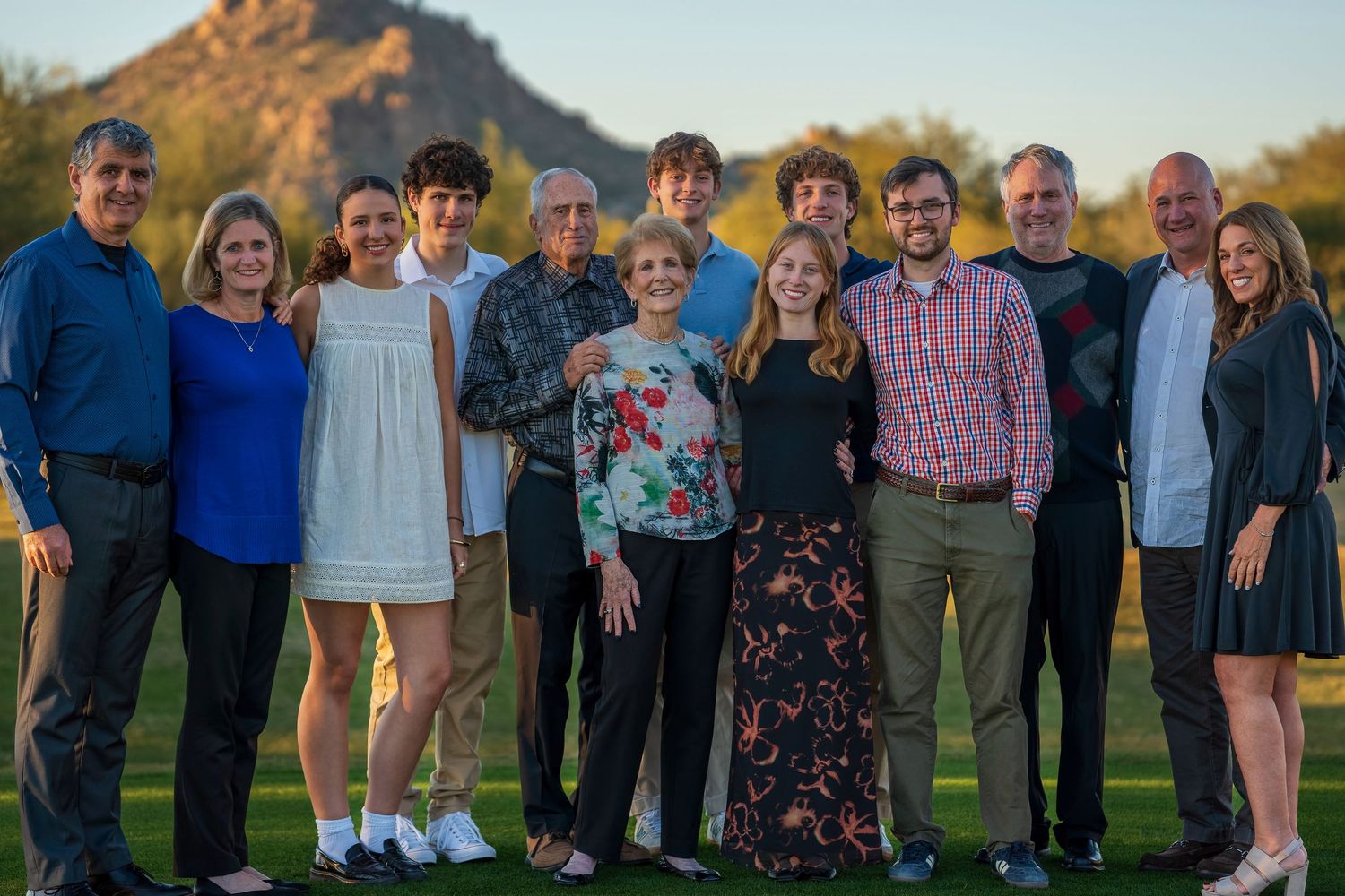 Extended family gathering for outdoor portraits on grass with mountain scenery in background.