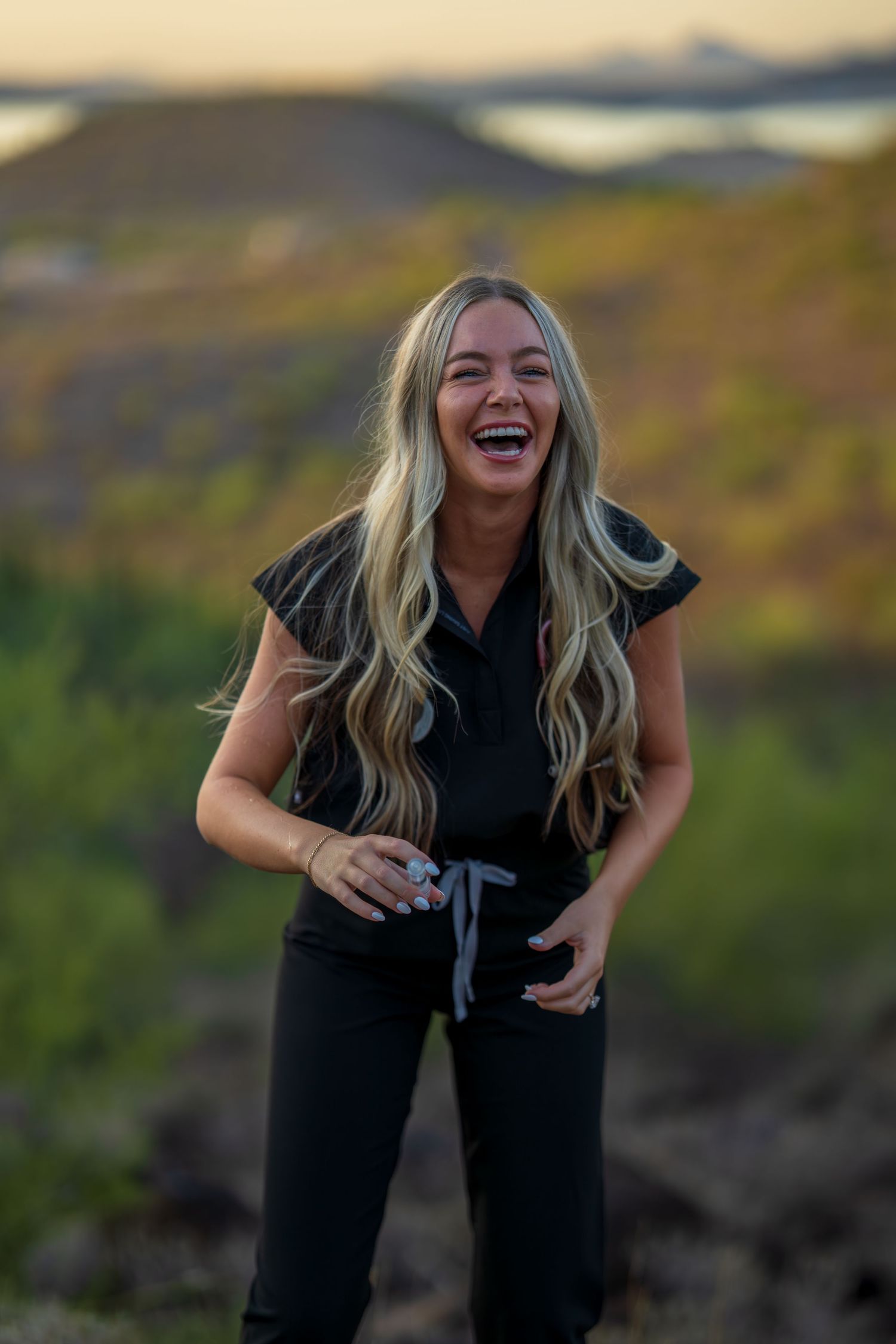 Healthcare worker in black uniform displays joyful expression during desert sunset photo session.