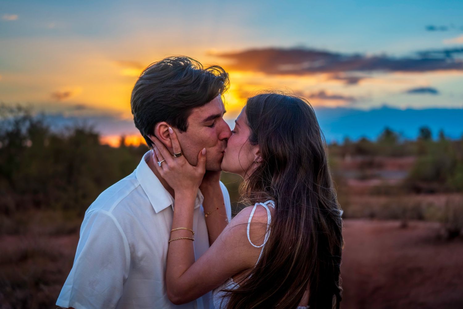 Romantic sunset kiss with dramatic sky backdrop in desert setting.