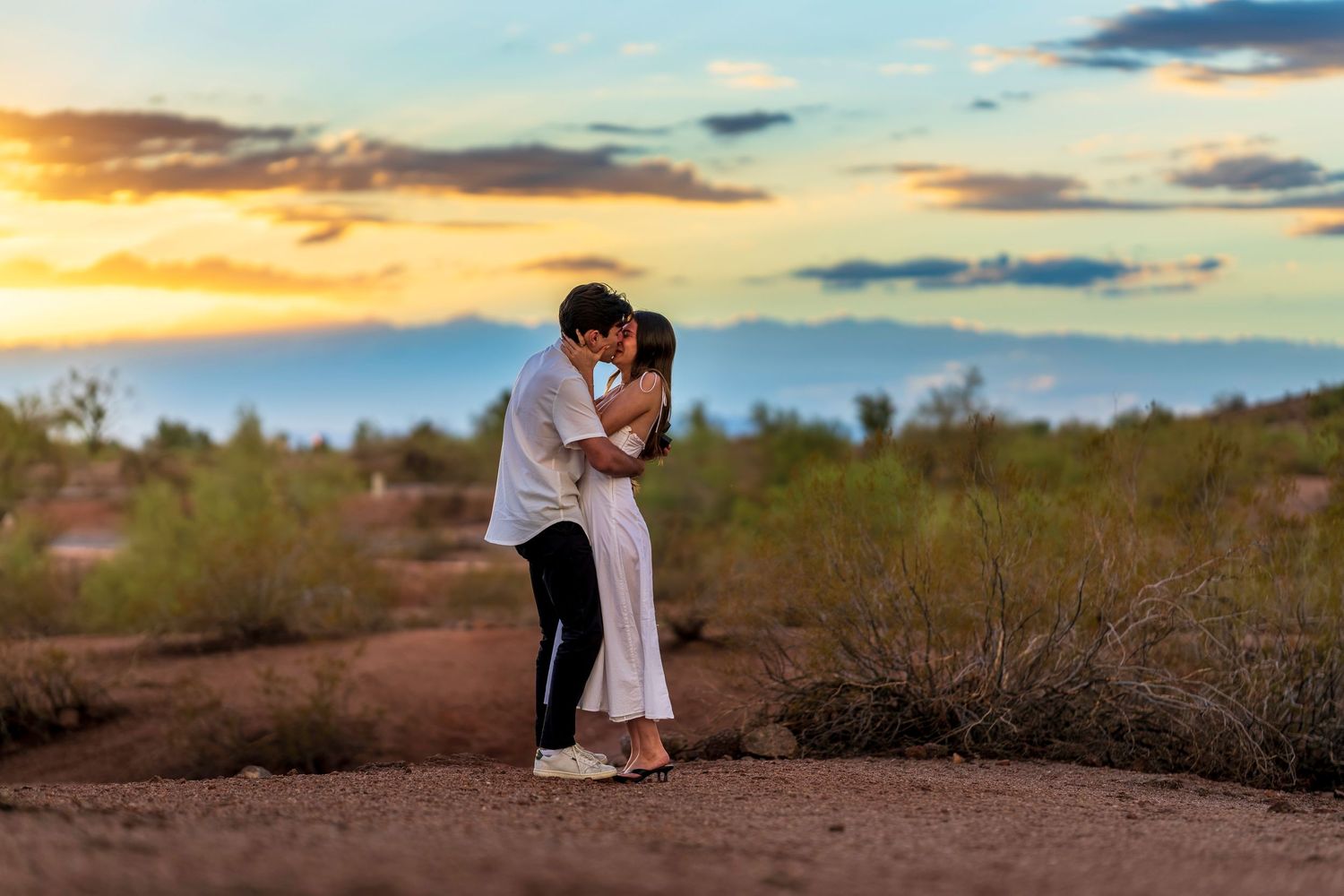 Two people share an intimate moment against a dramatic desert sunset backdrop.