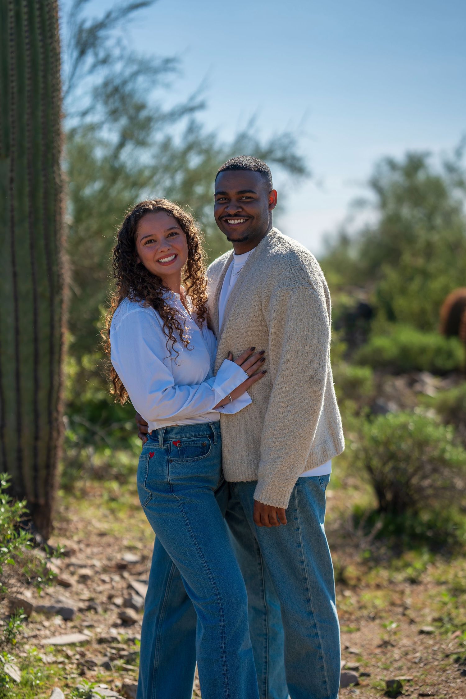 A couple shares a joyful moment on a desert hiking trail with cacti in the background.