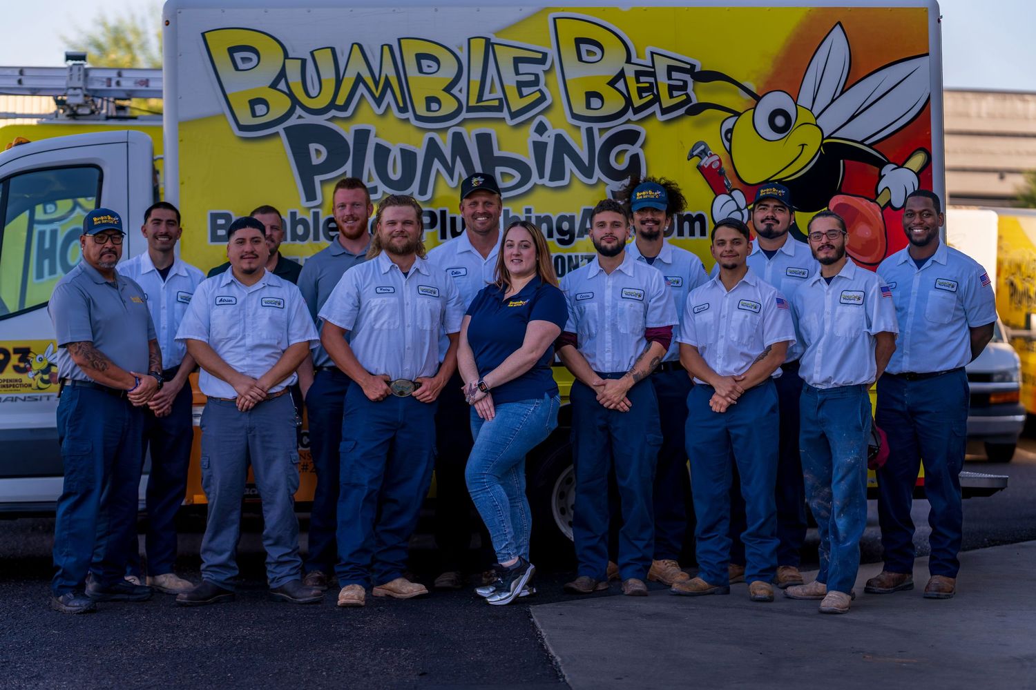 Group photo of plumbing company employees standing in front of bright yellow Bumble Bee Plumbing branded vehicles.