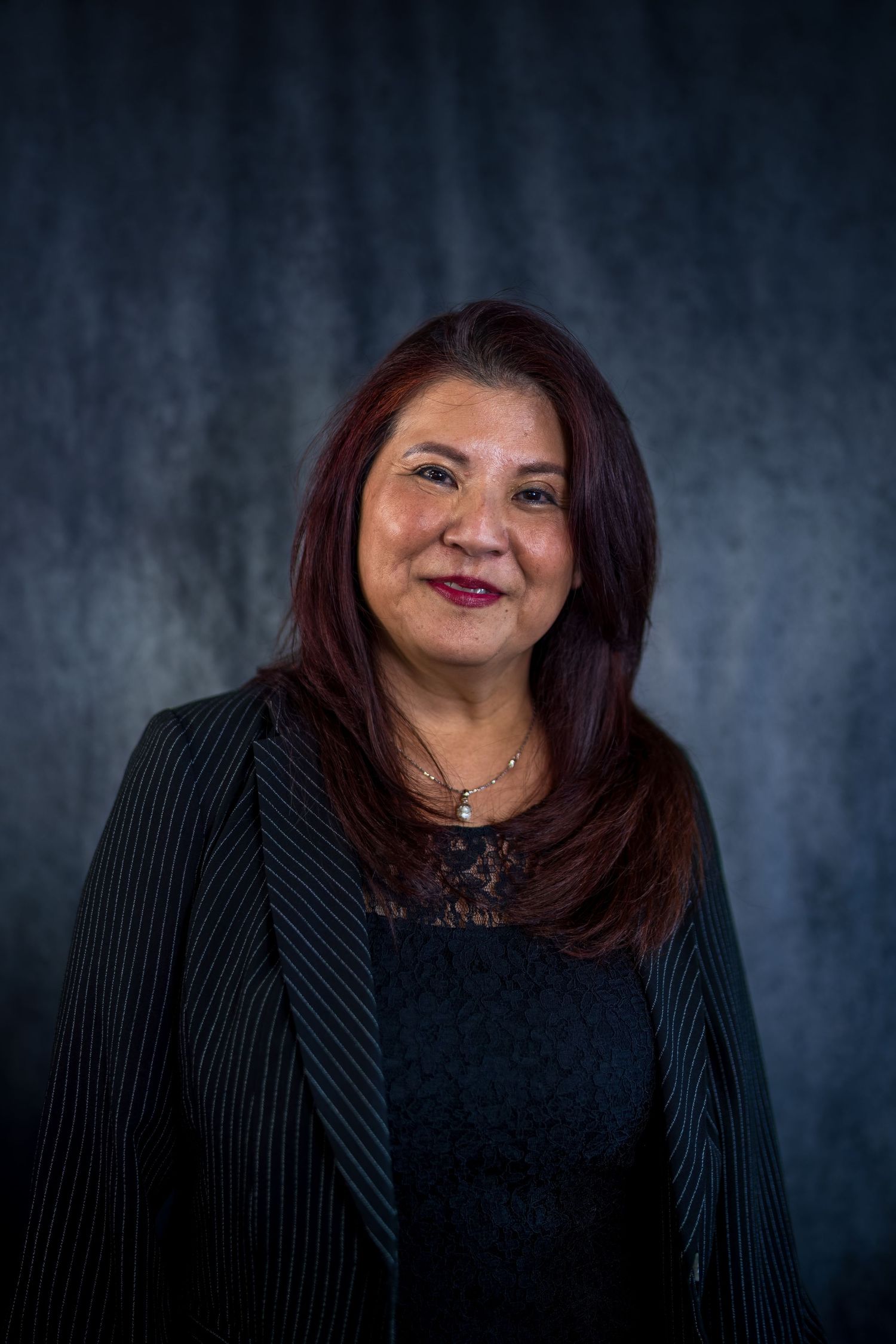 Business portrait with genuine smile wearing dark outfit against textured backdrop.