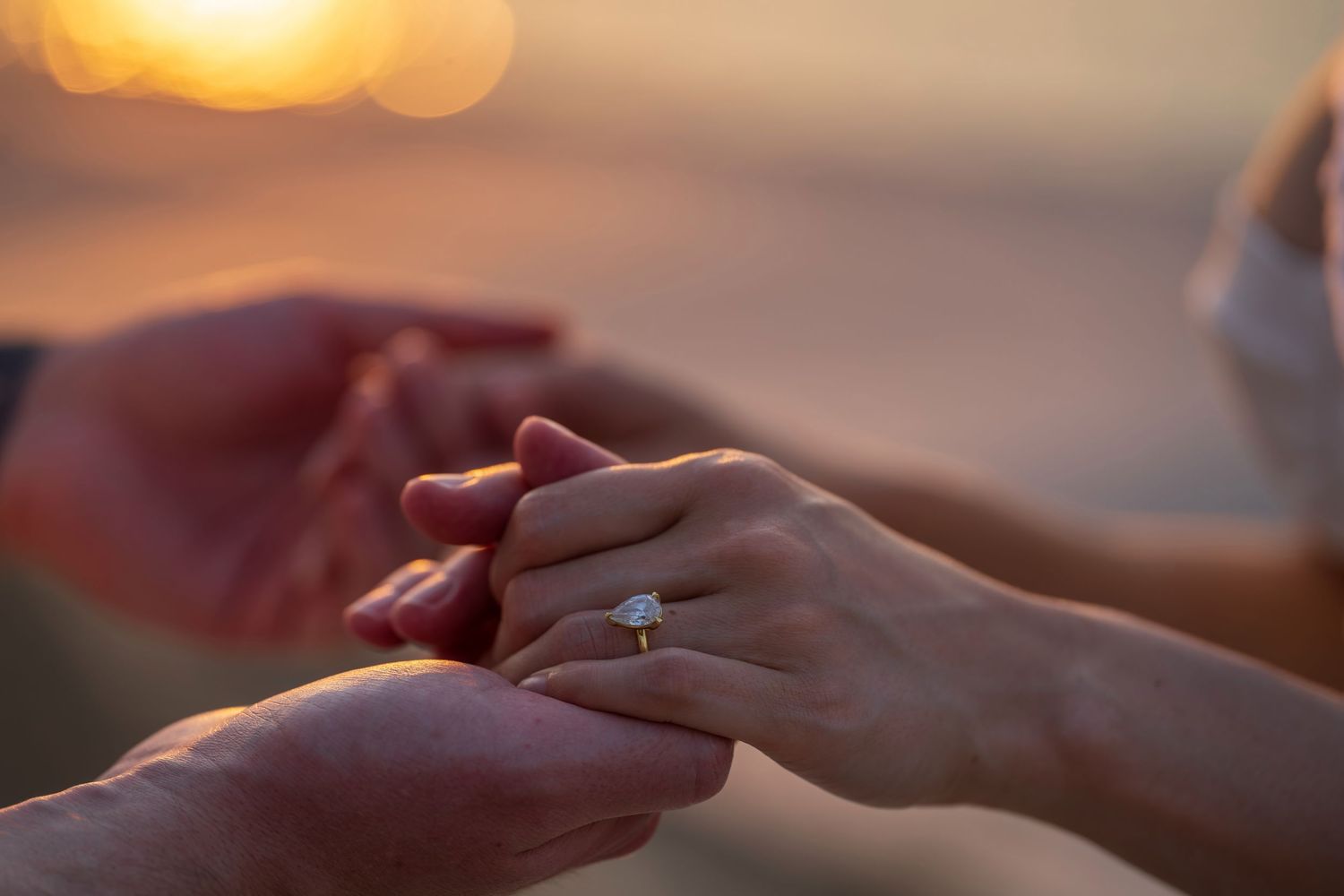 Close-up of hands exchanging rings during golden hour.