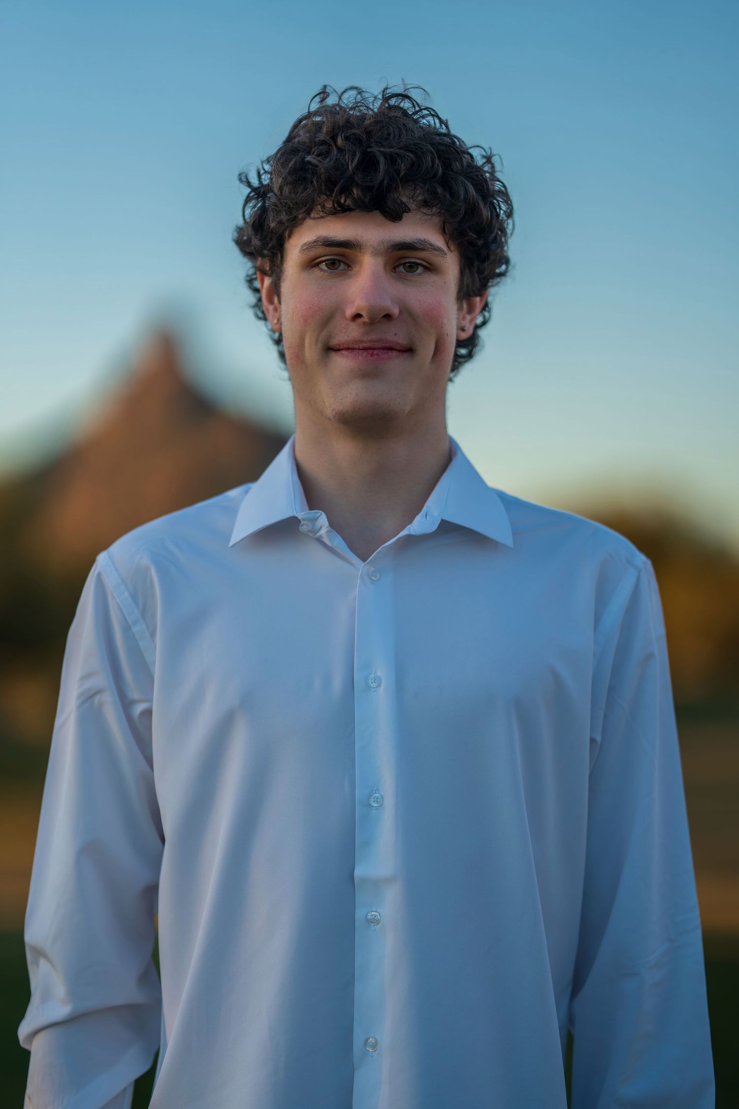 Portrait of person in white button-down shirt against blue evening sky.
