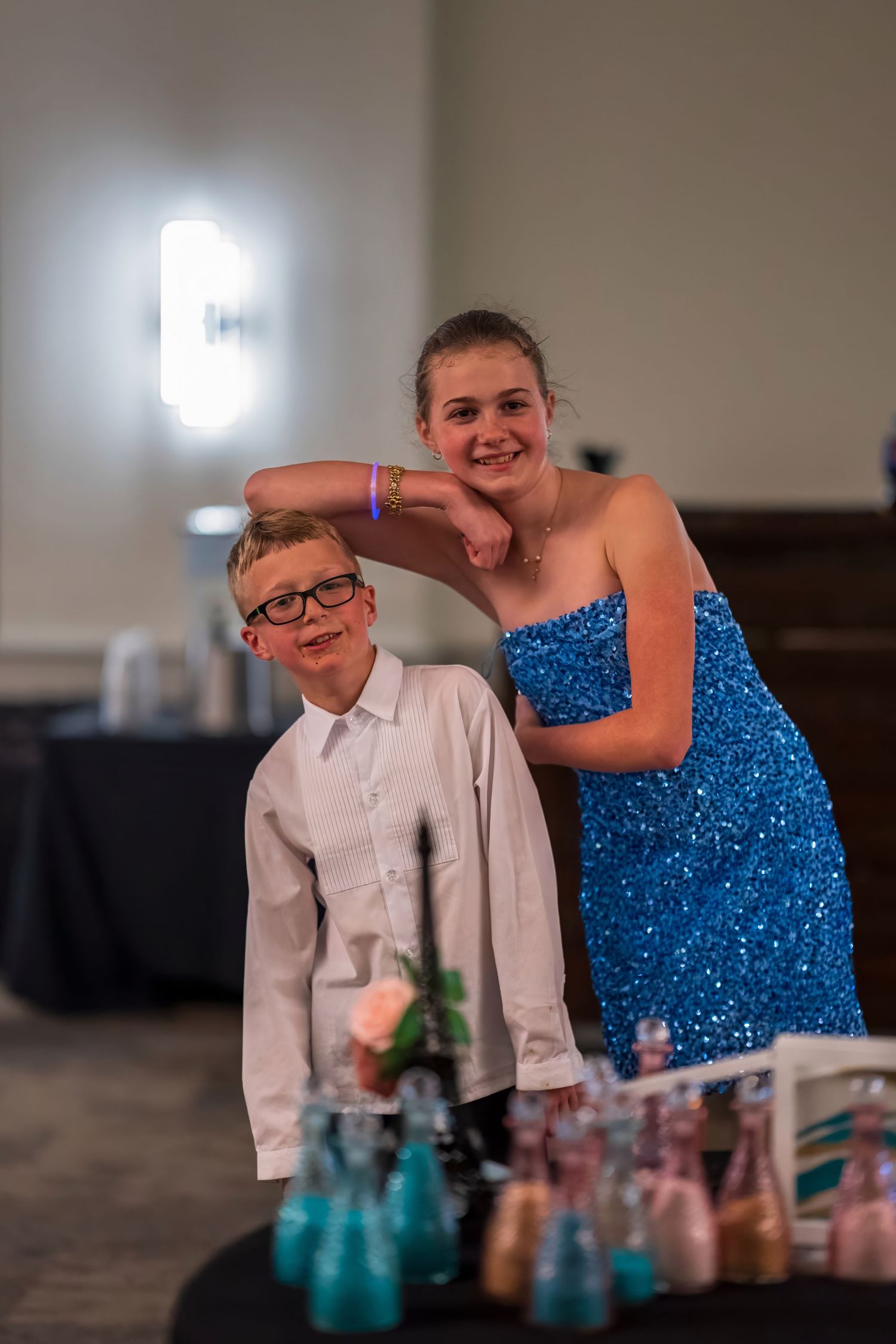 A young boy in a white shirt and a girl in a blue sequined dress pose together at a formal event.