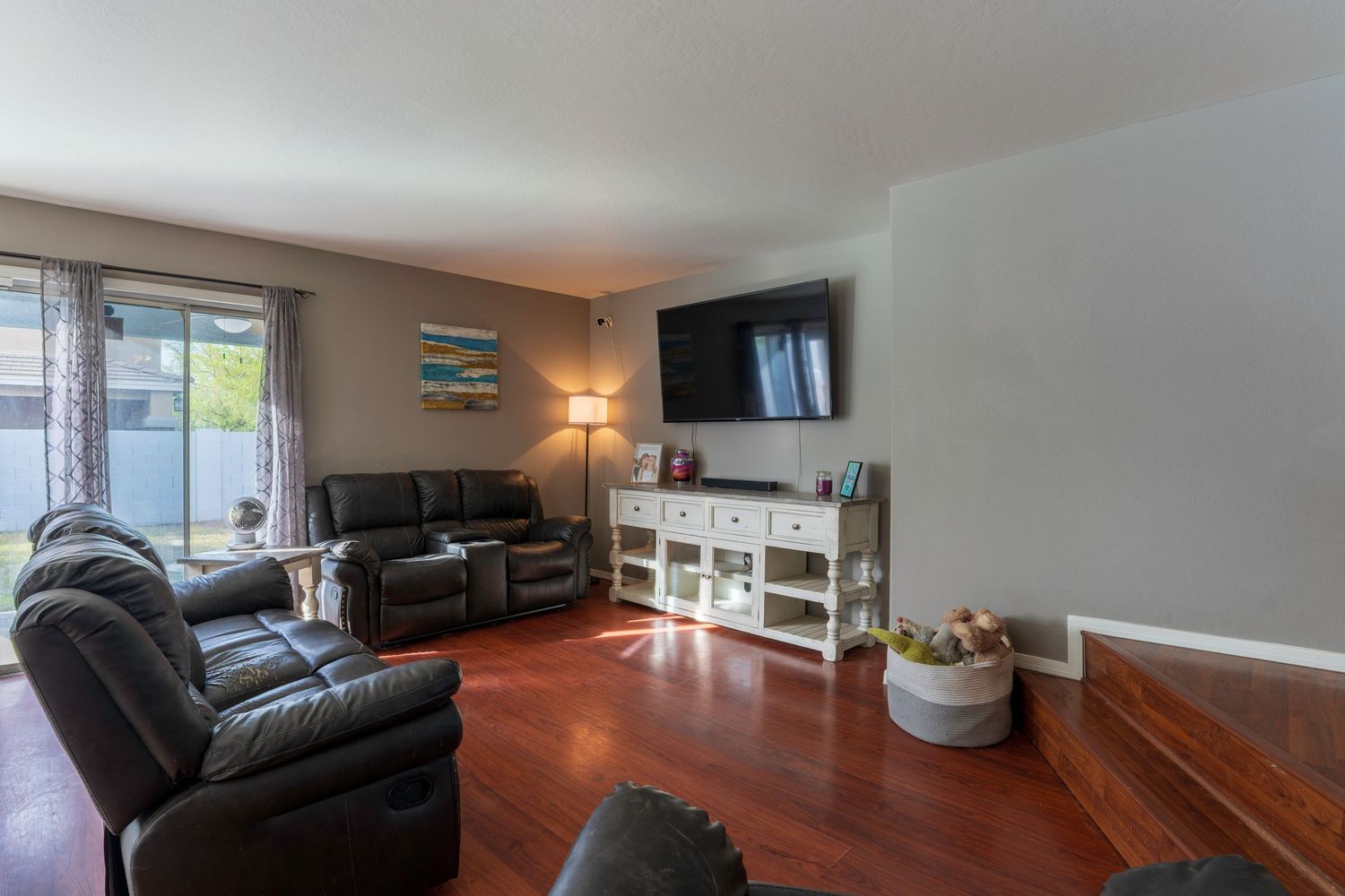 Cozy living room with leather recliner sofas, hardwood floors, wall-mounted TV, and a white storage console near a bright window.