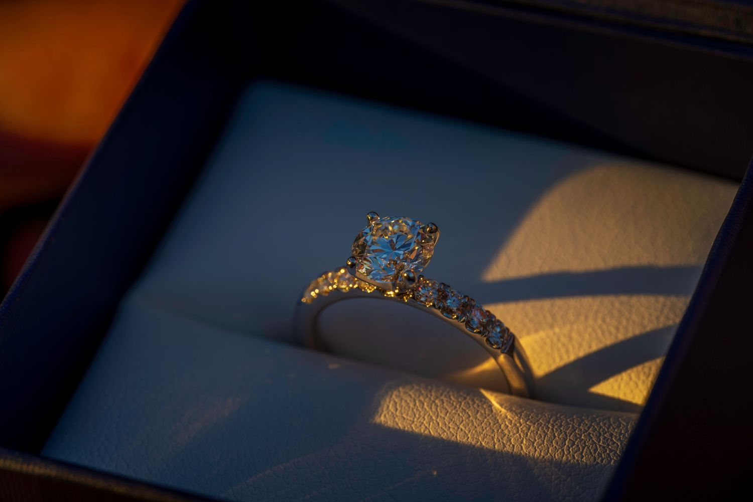 Close-up of a diamond engagement ring with halo setting in a blue velvet jewelry box.
