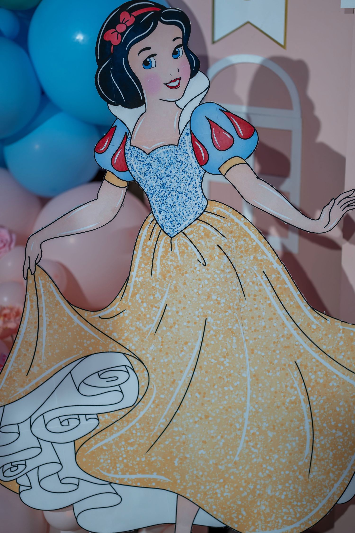 Disney princess cutout in a yellow and blue dress with short puffed sleeves against blue balloons.