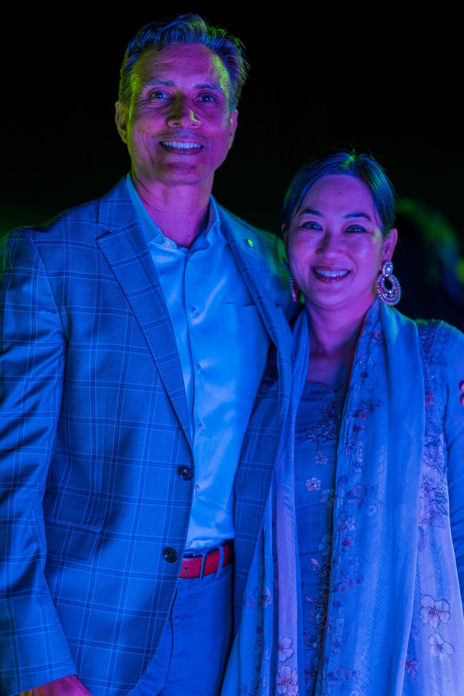 Couple posing together under blue and purple party lights wearing formal attire.