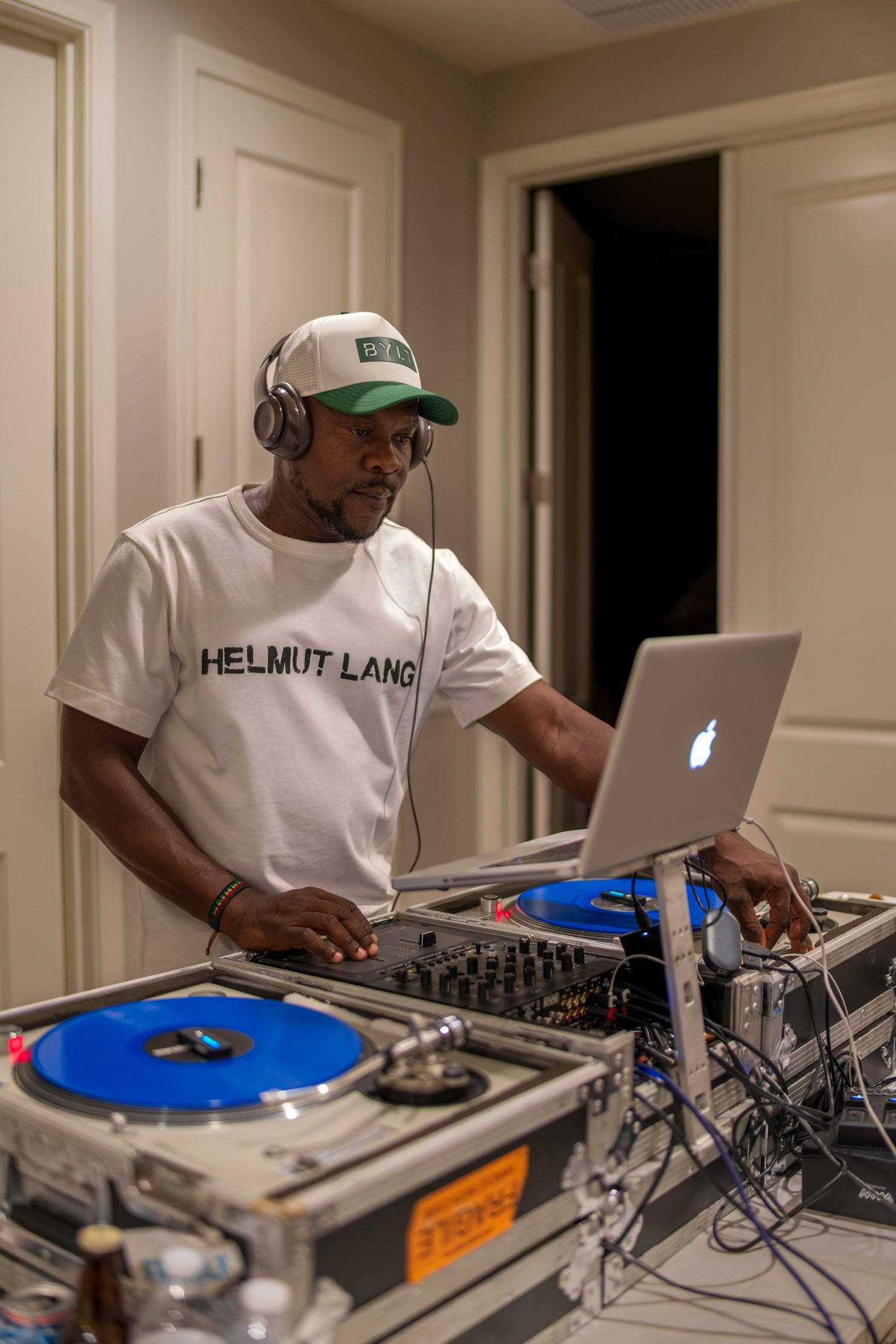 DJ in Helmut Lang shirt mixing music on turntables with laptop at a private party.