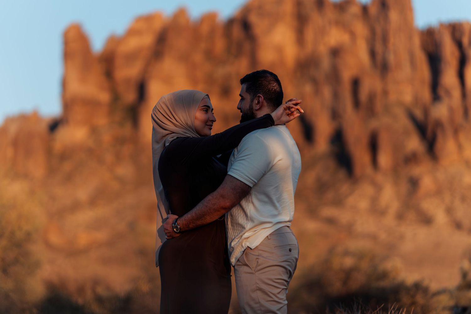 A couple embraces tenderly at golden hour with dramatic desert rock formations in the background.