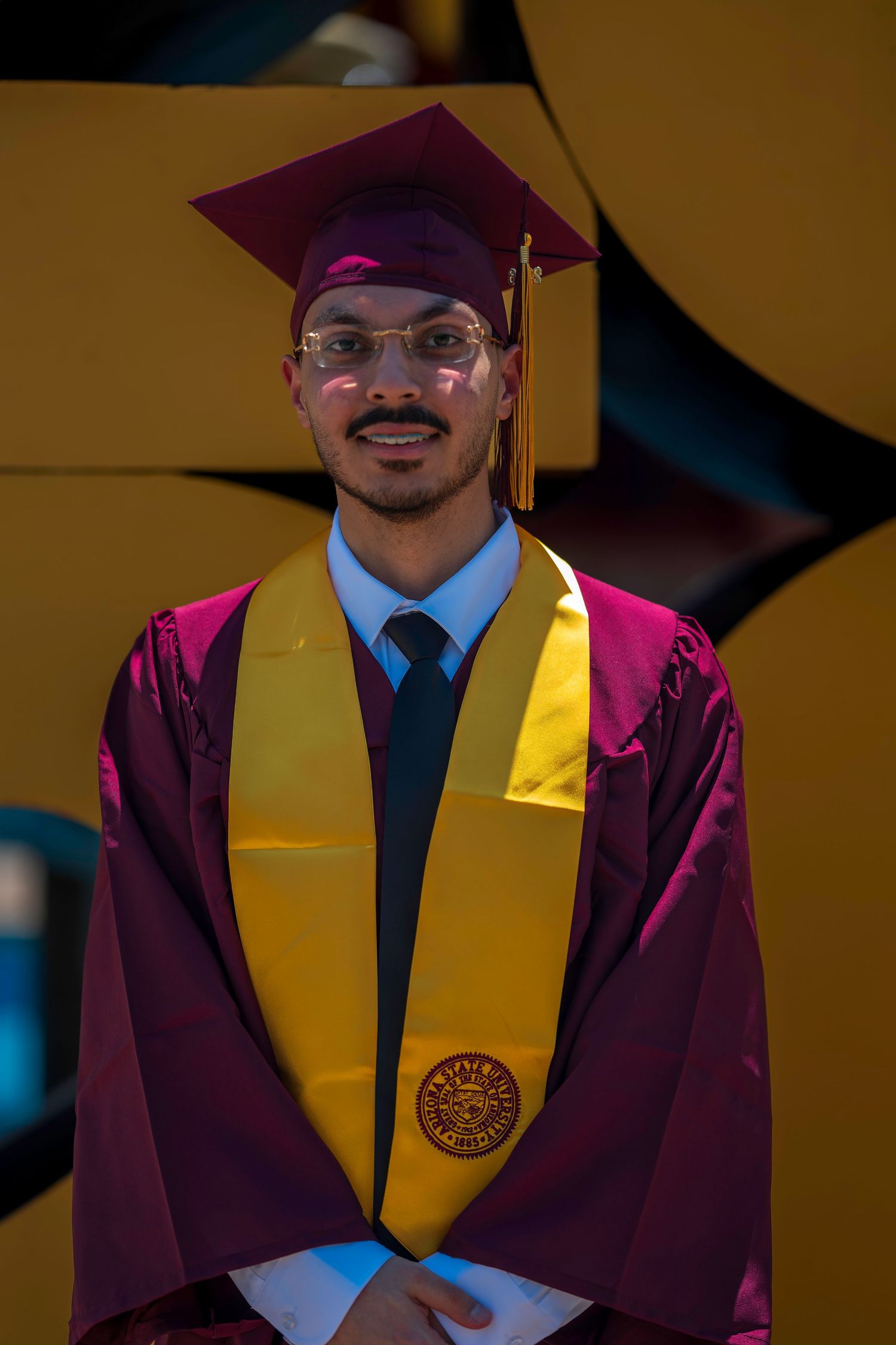 Graduate in maroon and gold cap and gown smiling at graduation ceremony.