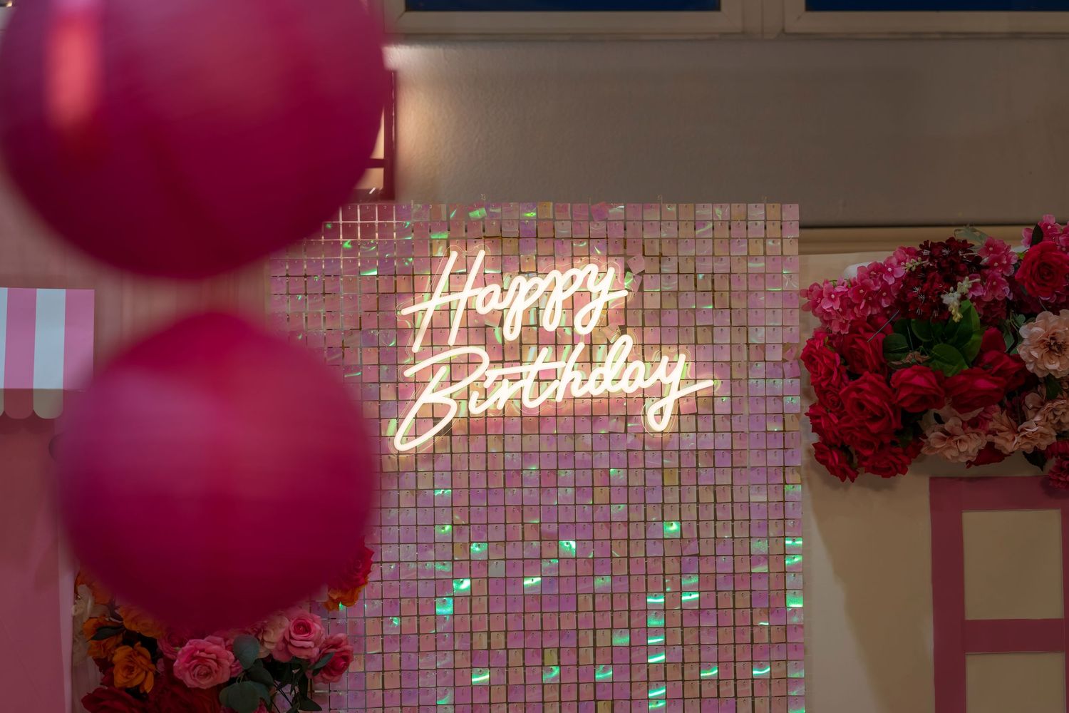 Glowing neon birthday sign against a pink decorated wall with balloons.