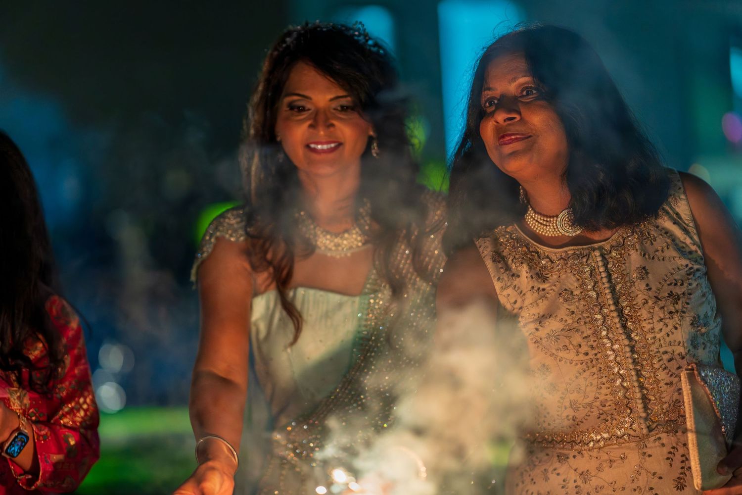 Two people in formal attire smile while holding sparklers amid smoke effects.