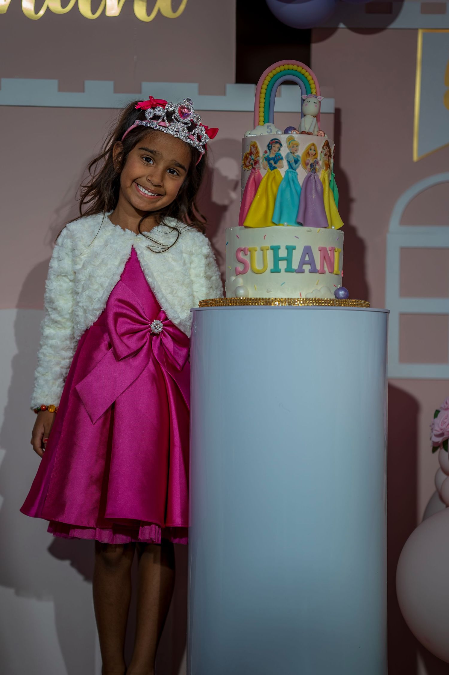 A festive birthday cake with rainbow tassels and decorative elements displayed on a white pedestal.