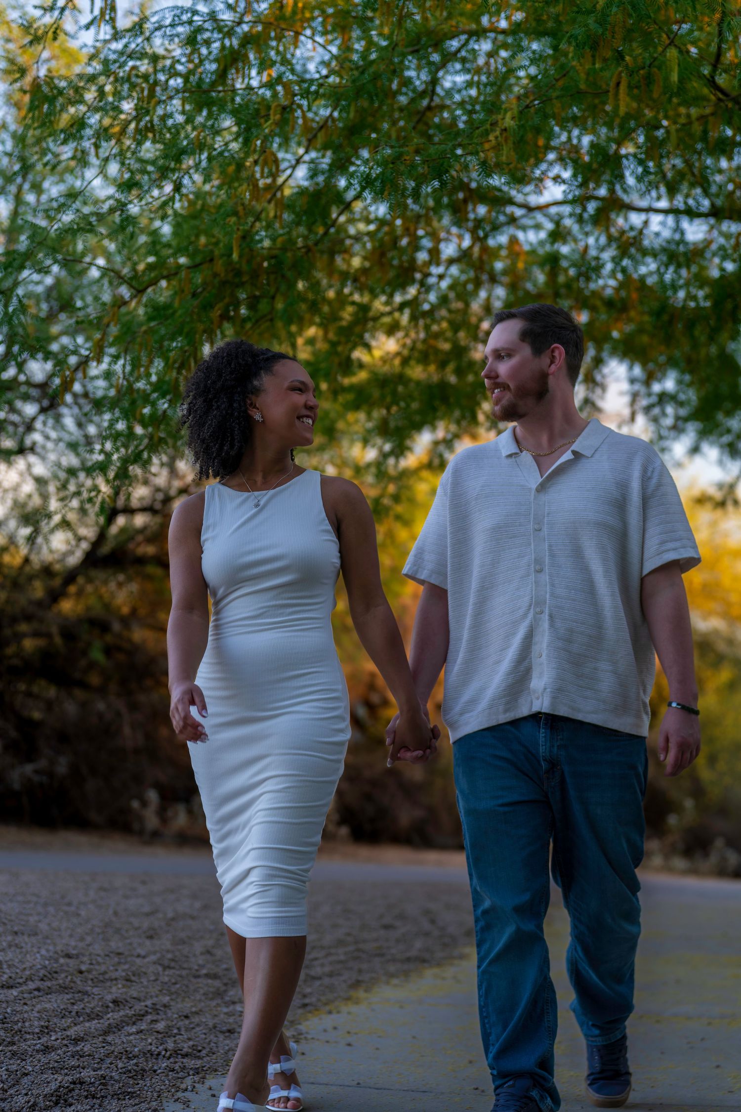 Happy interracial couple holding hands and smiling while walking together outdoors among autumn trees.