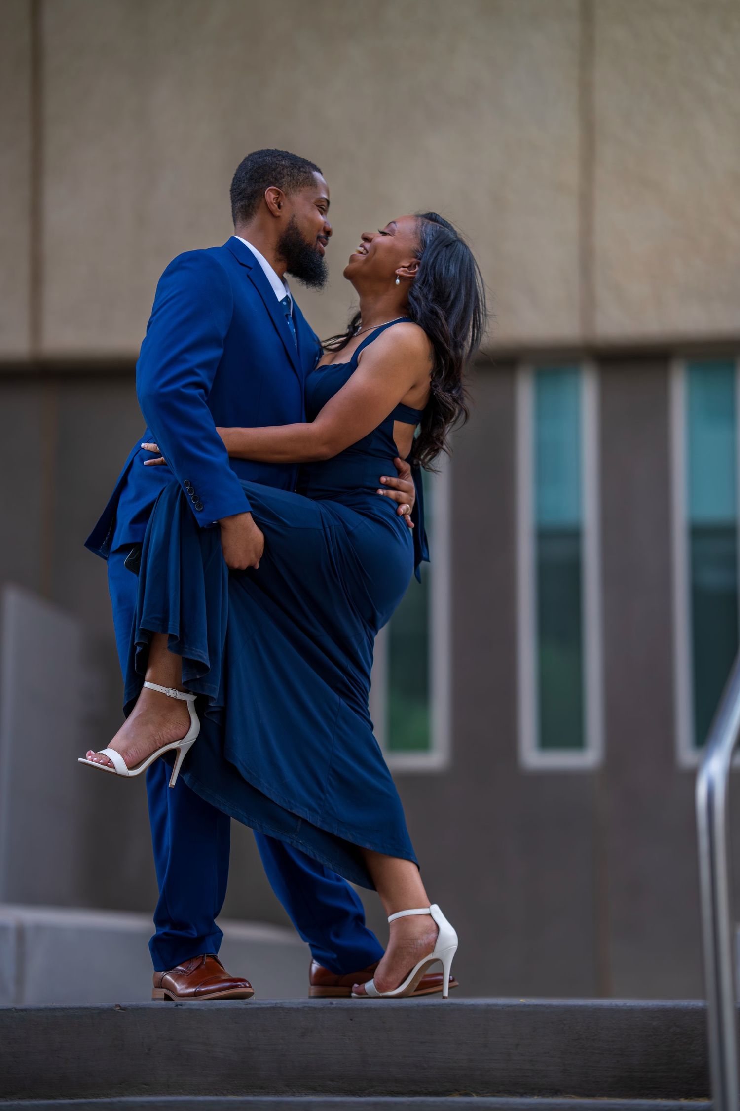 Couple in matching blue outfits share romantic dance pose on steps of modern building.