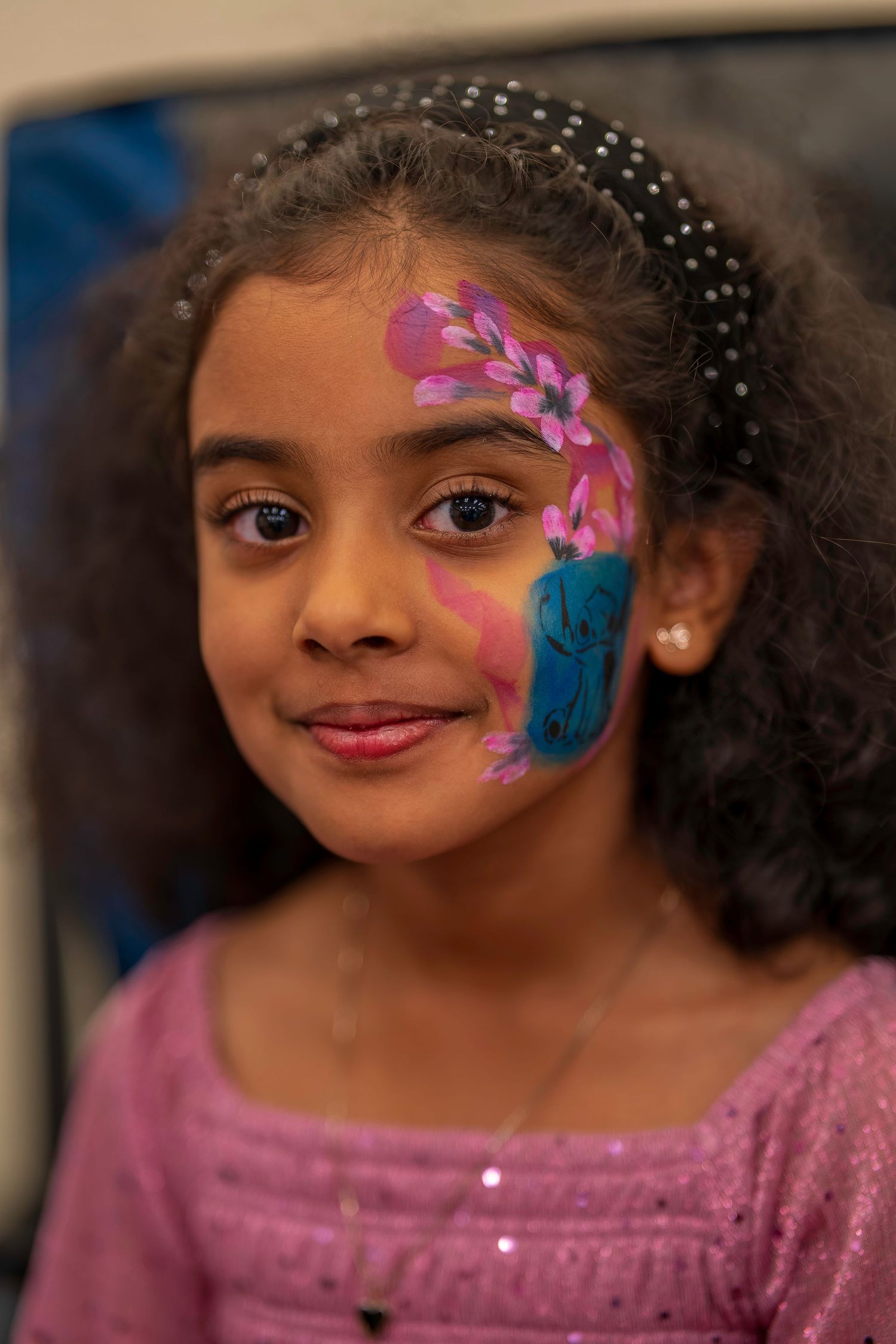Young girl with colorful floral face paint smiling at birthday celebration.
