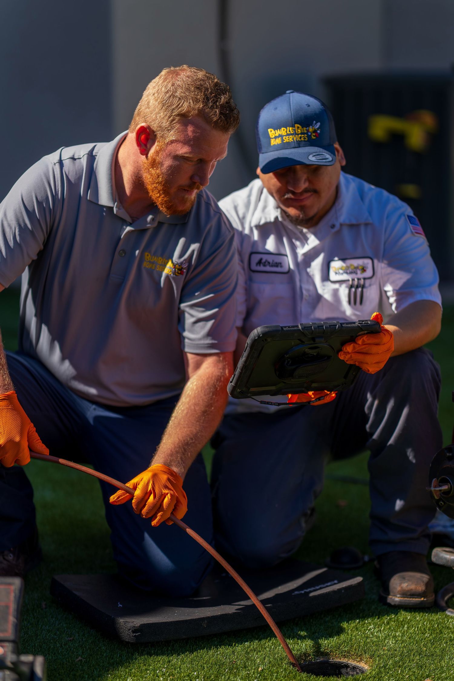 Professional plumbers examining equipment while crouched on grass outdoors.