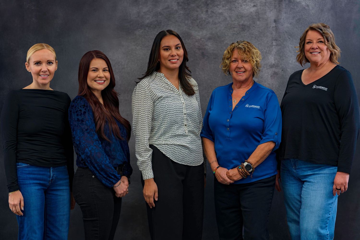 Group of employees in coordinated blue and black attire stand together for company photo.
