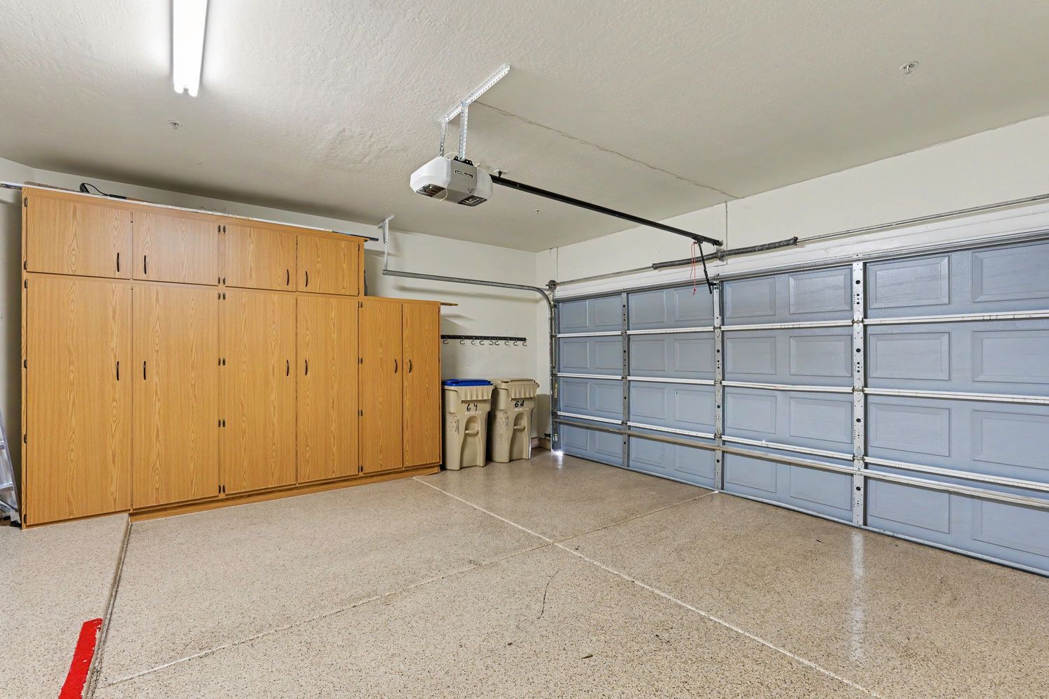 Spacious two-car garage with epoxy floors, built-in wooden cabinets, and automatic garage door opener.