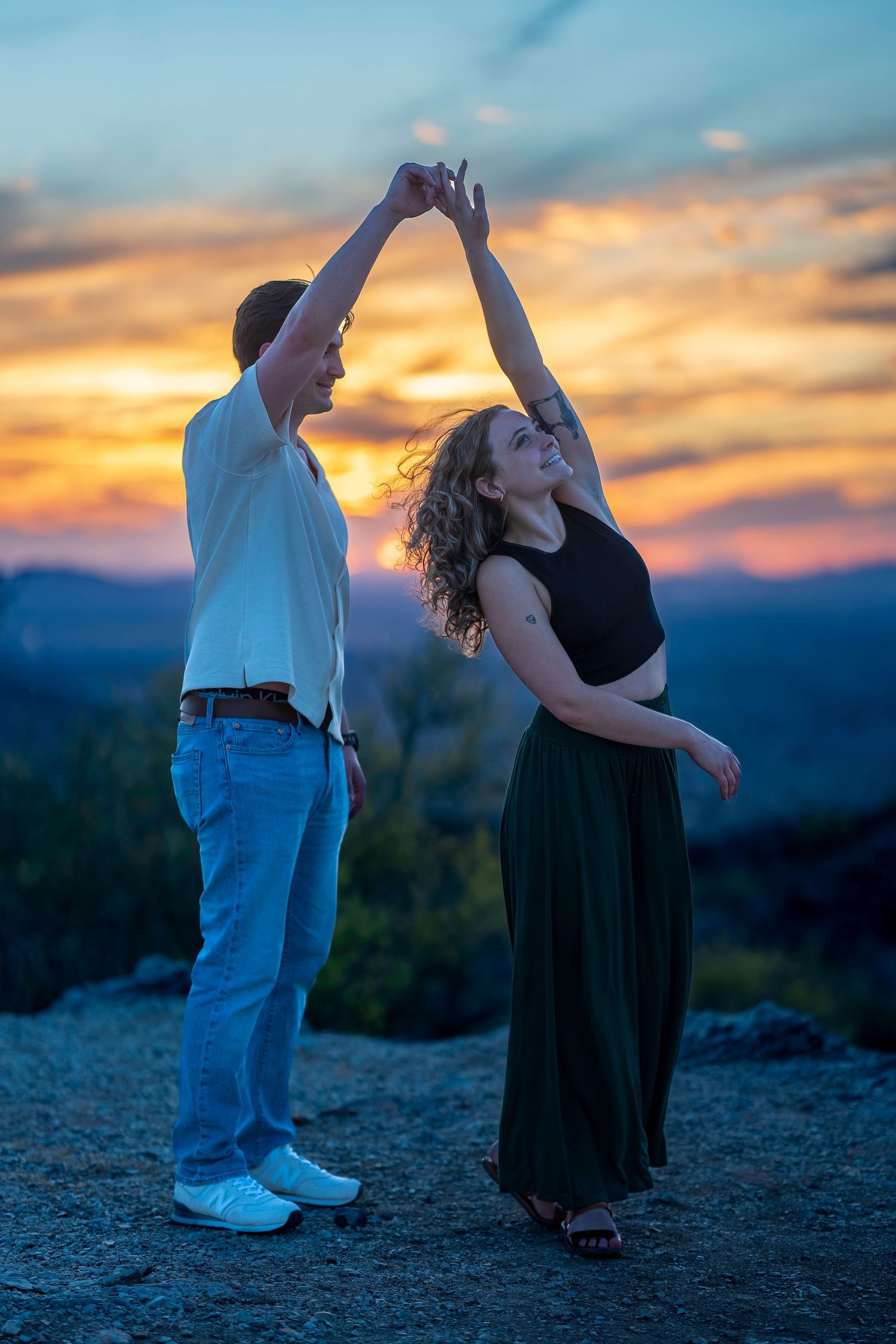 Joyful couple dancing and spinning together against a dramatic colorful sunset sky.