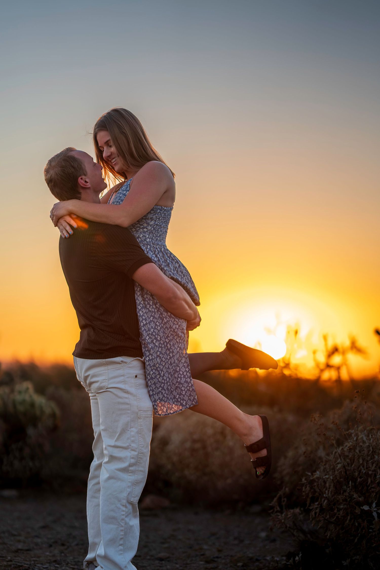 A man lifts his partner during a romantic sunset embrace outdoors.