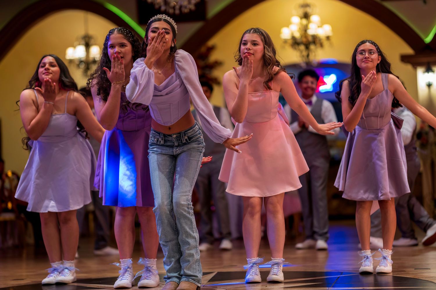 Five young women in lavender dresses and jeans dance expressively at a formal quinceañera celebration.