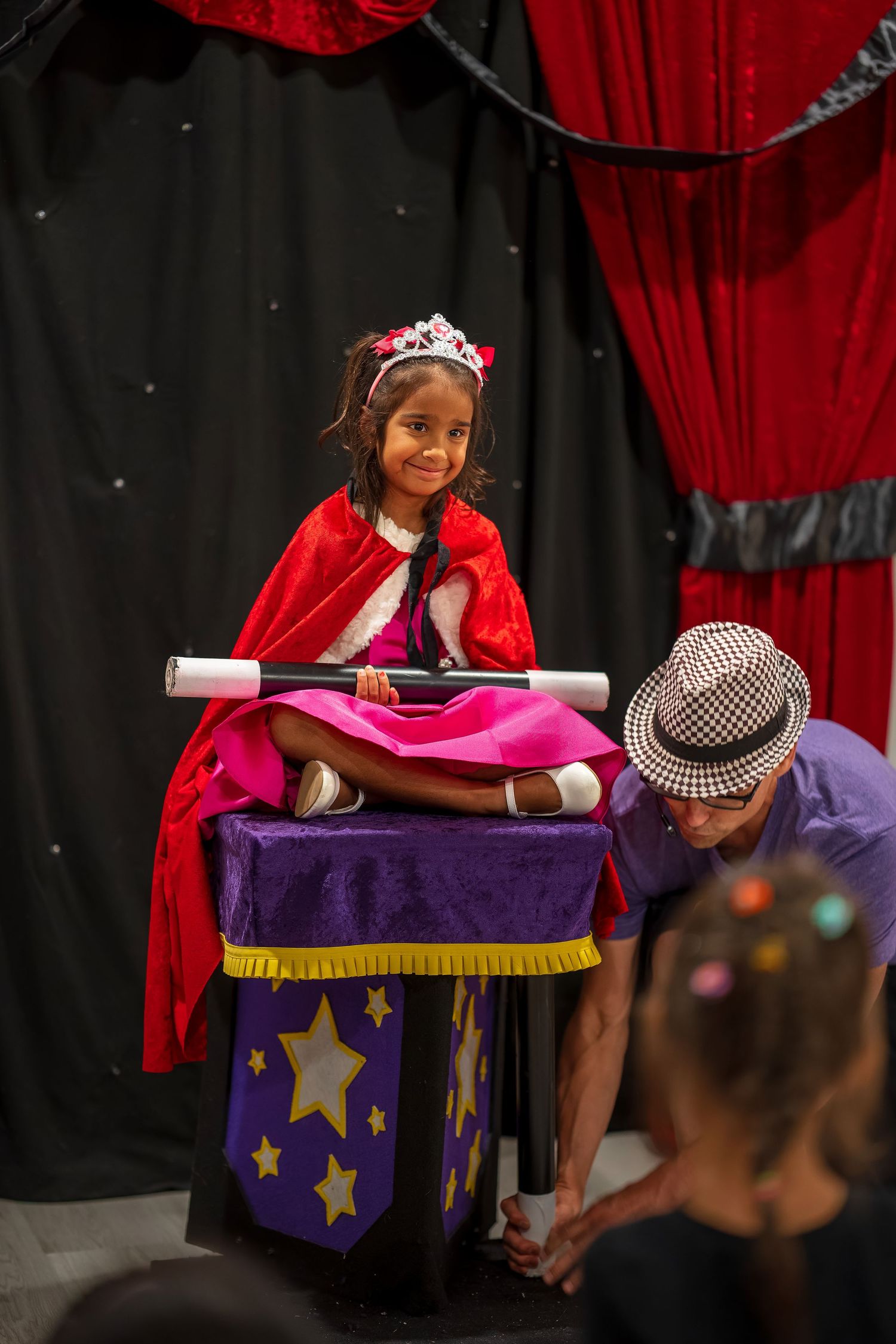 Magic performance featuring a decorated purple table with gold stars and red curtain background.