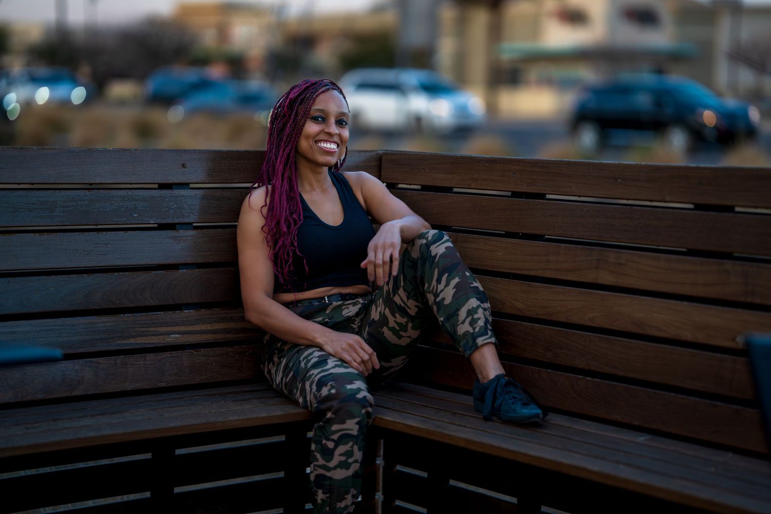 Casual outdoor portrait on wooden bench with city lights in background.
