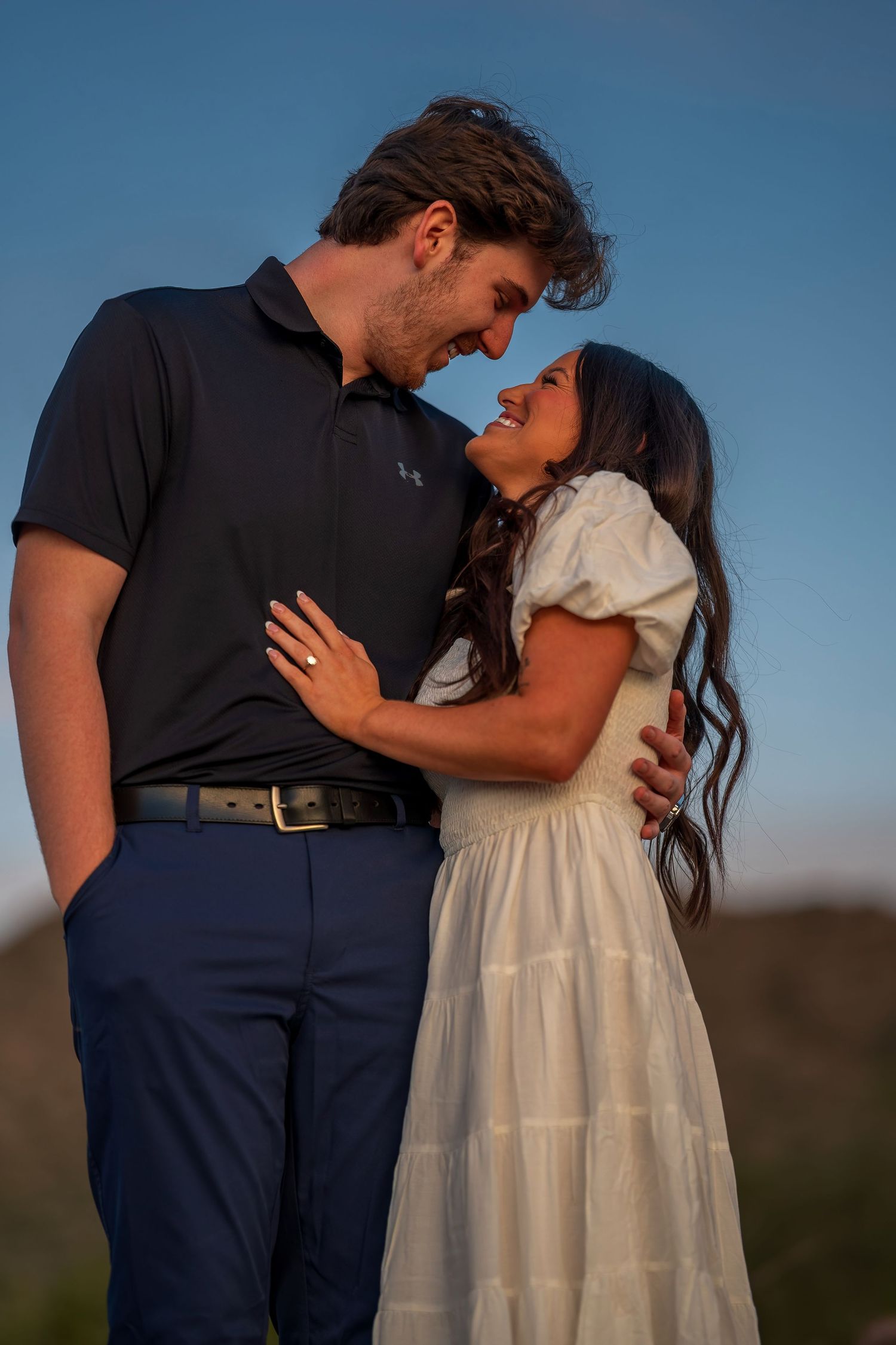 A romantic couple embraces during a sunset photoshoot in the desert with mountains in the background.