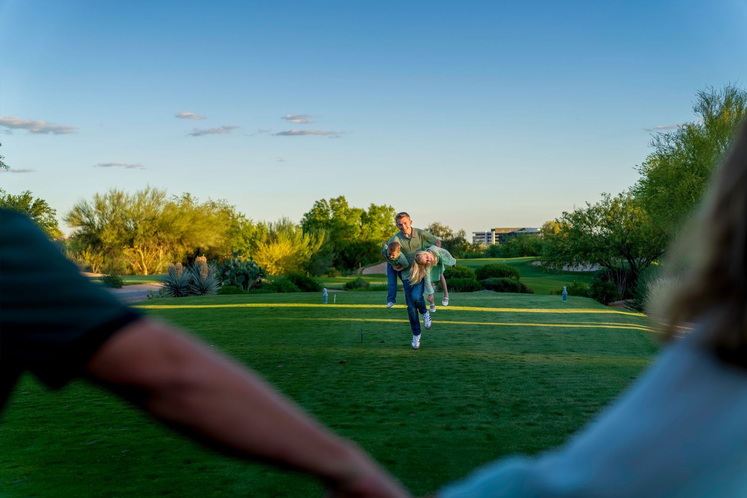 Father running across green lawn toward family during outdoor photo session at sunset.