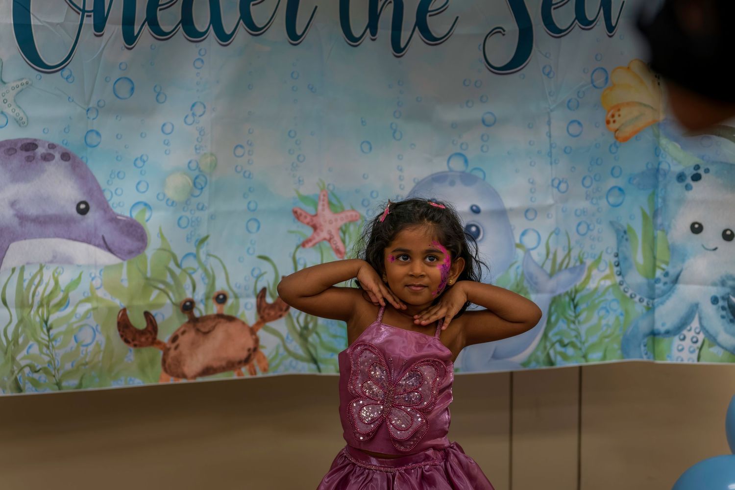 Young girl in purple dress posing in front of Under the Sea themed backdrop.