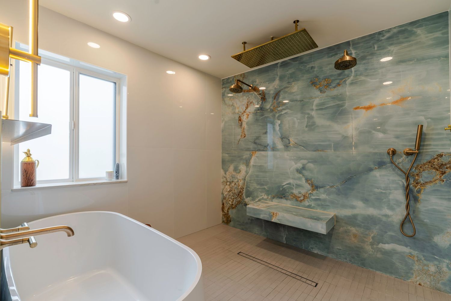 Luxurious bathroom with freestanding tub, gold fixtures, and stunning blue marble shower wall with built-in bench.