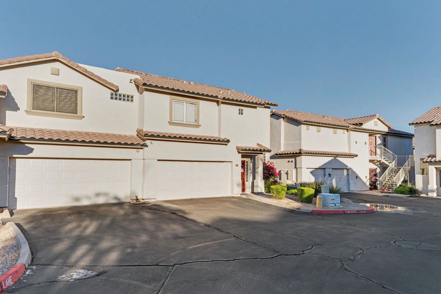 White stucco townhomes with two-car garages and terracotta tile roofs in a sunny residential complex.