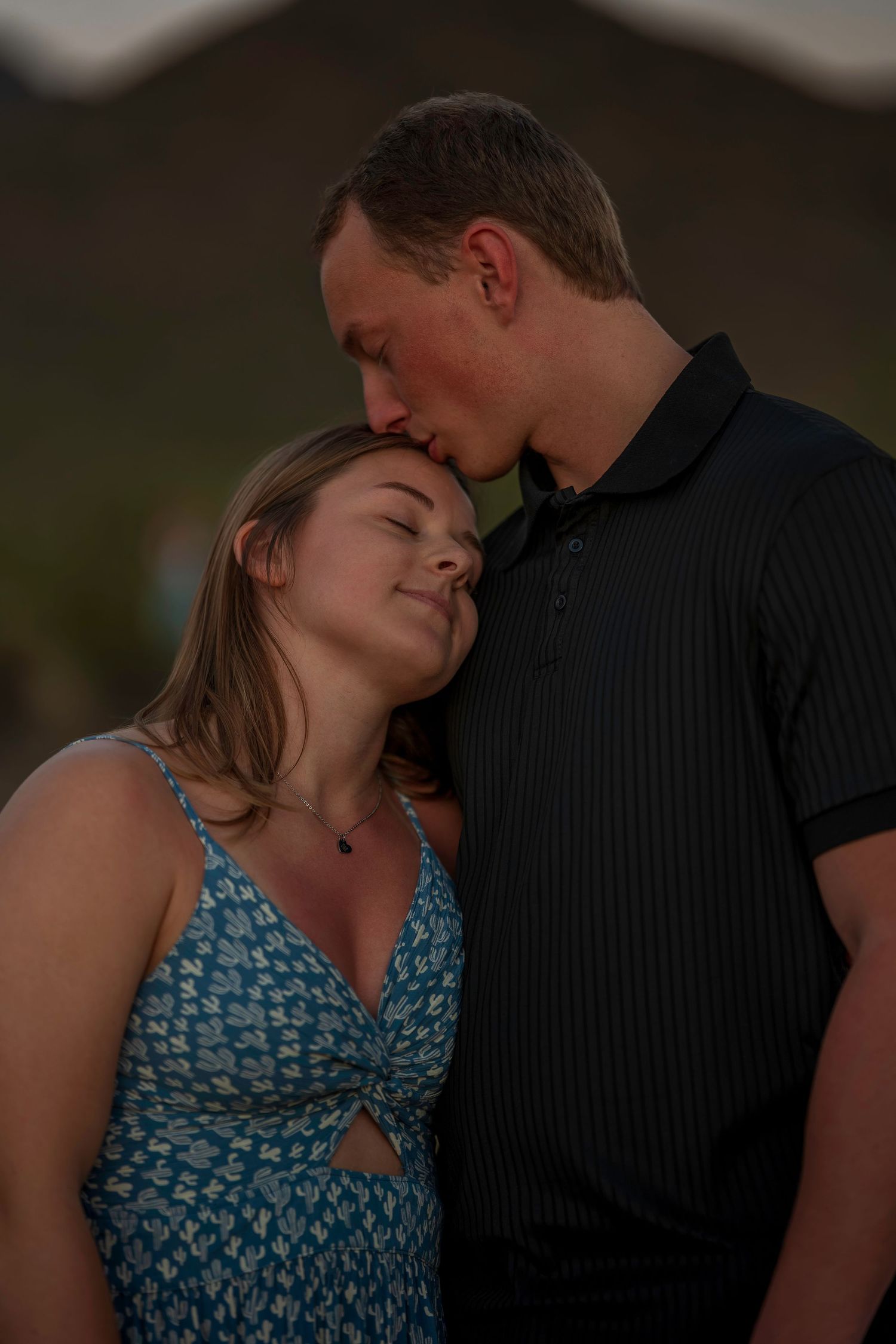 Couple sharing tender moment, man kissing womans forehead at dusk outdoors.
