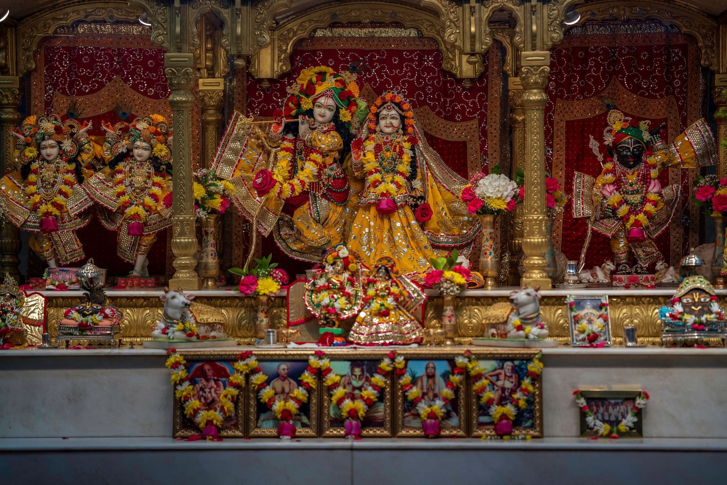 Ornate Hindu temple altar with colorful deity statues adorned in floral garlands and gold decorations.