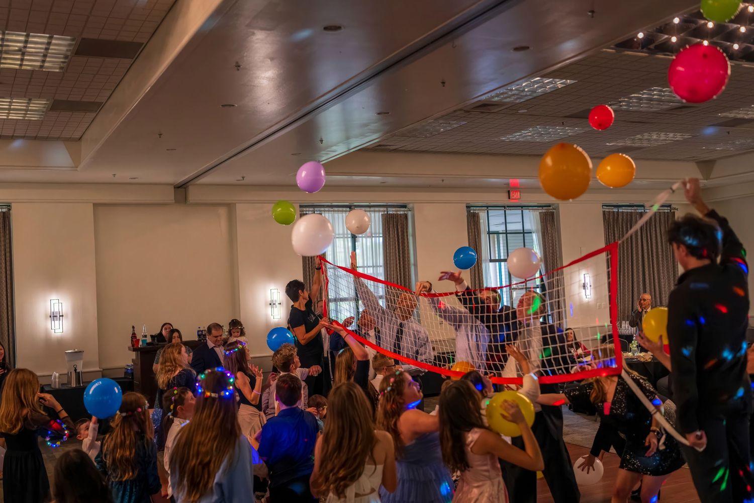 Children celebrating at a colorful party with balloons, streamers, and glowing accessories in a festive indoor venue.