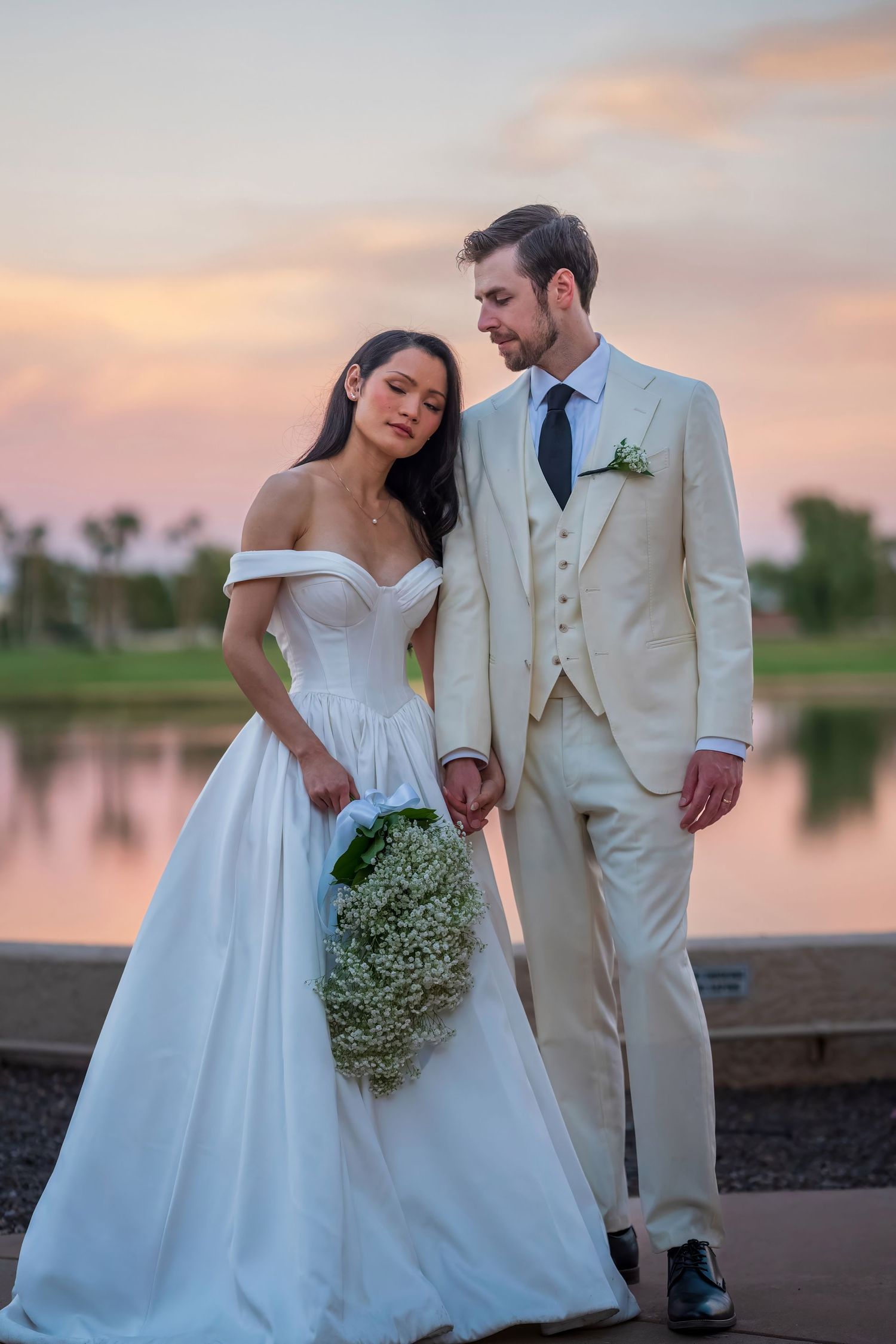 Wedding couple poses with baby's breath bouquet against pink sunset sky.