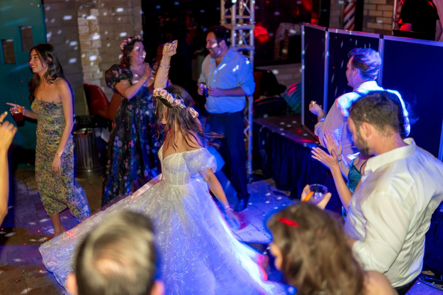 Wedding guests celebrate on the dance floor with the bride in a sparkling gown and floral crown.