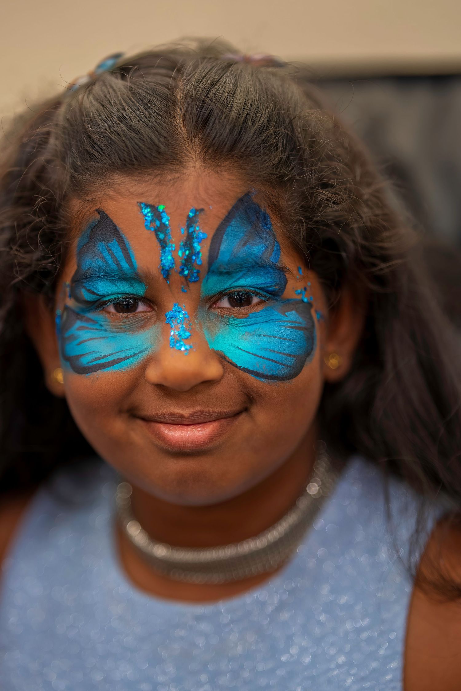 A young girl with a vibrant blue butterfly face paint design smiles at the camera.